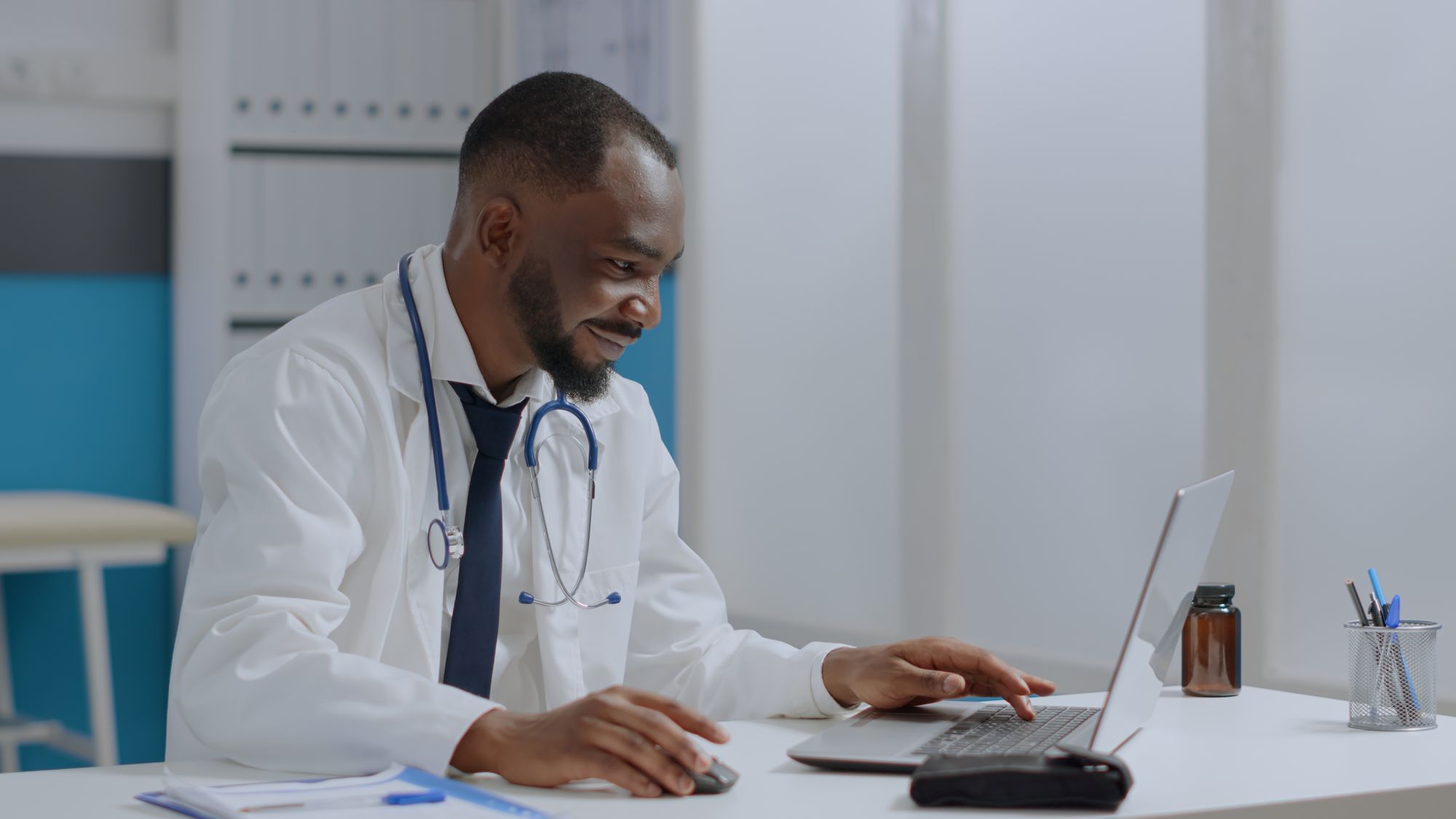 A doctor typing notes on a laptop in his consulting room