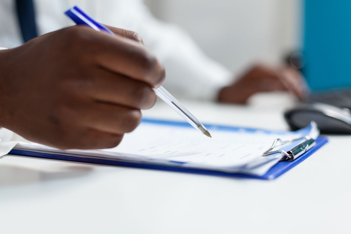 A doctor writing a prescription by hand on a paper clipboard